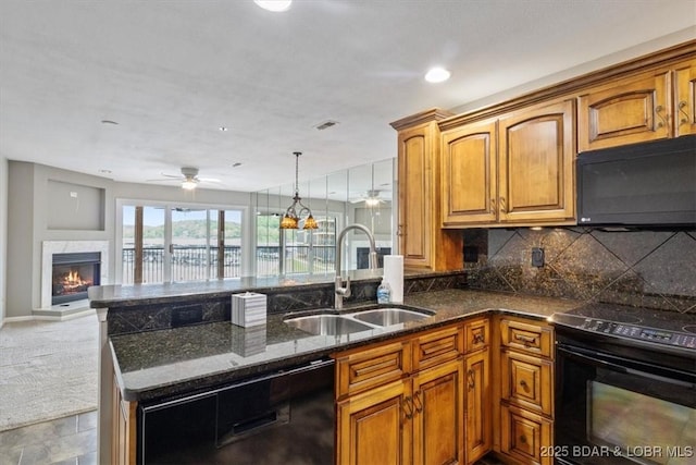 kitchen featuring black appliances, a sink, brown cabinets, dark stone countertops, and a lit fireplace