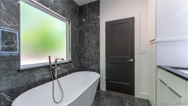 bathroom featuring marble tiled floors, a soaking tub, and vanity