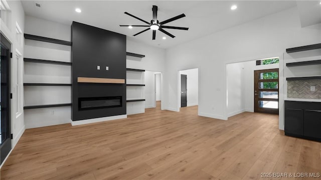 unfurnished living room featuring a large fireplace, light wood-style floors, recessed lighting, a towering ceiling, and baseboards