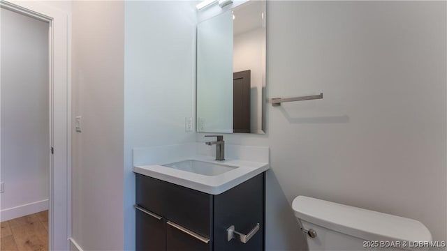 half bathroom with toilet, vanity, and wood finished floors