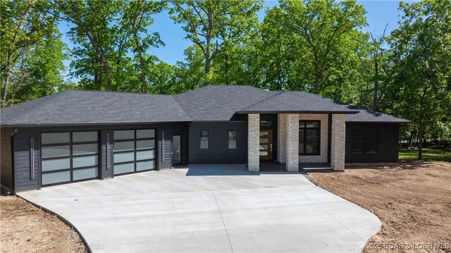 view of front of house with concrete driveway, a garage, and roof with shingles