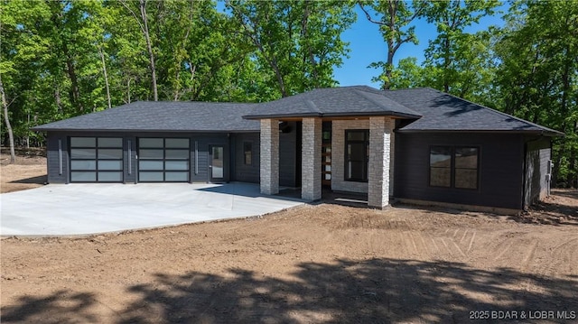 view of front of house with a garage, concrete driveway, and a shingled roof