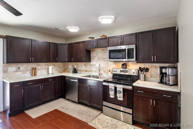 kitchen featuring stainless steel appliances, a sink, light countertops, decorative backsplash, and dark brown cabinets