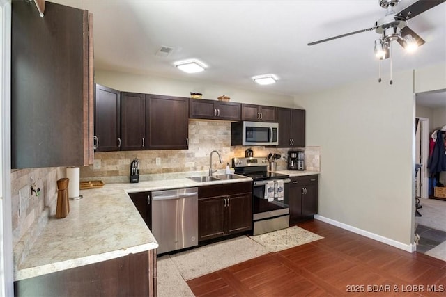 kitchen with appliances with stainless steel finishes, a sink, ceiling fan, dark brown cabinets, and decorative backsplash