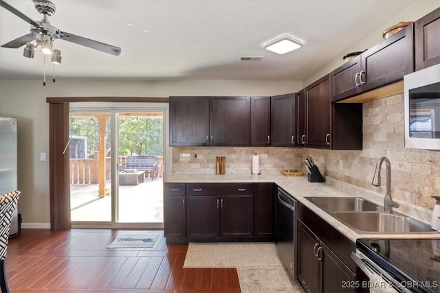 kitchen featuring appliances with stainless steel finishes, a sink, backsplash, dark brown cabinets, and light wood-type flooring