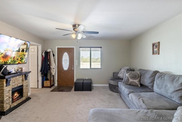 living area with carpet flooring, ceiling fan, a stone fireplace, and baseboards