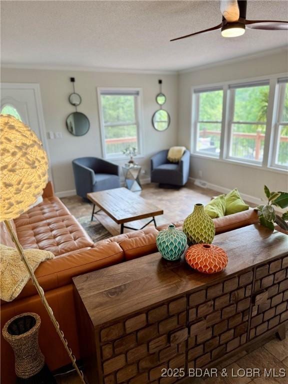 living room with plenty of natural light, ornamental molding, ceiling fan, baseboards, and a textured ceiling