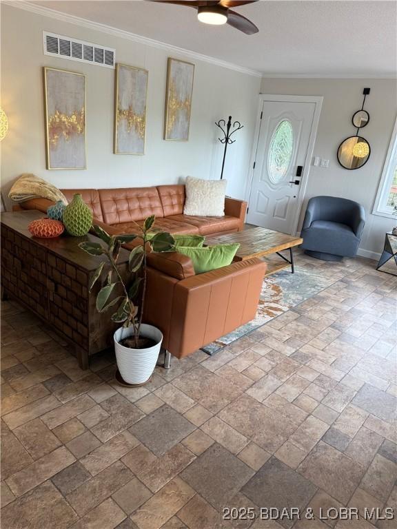 living room featuring crown molding, ceiling fan, stone tile flooring, and baseboards