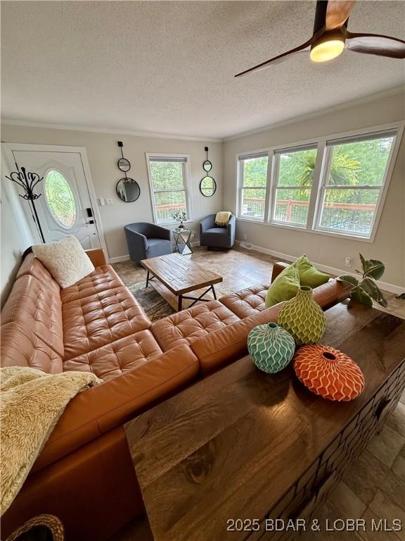 living area with a textured ceiling, baseboards, ceiling fan, and crown molding