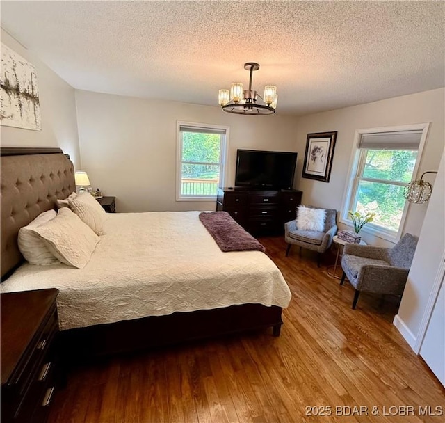 bedroom with wood finished floors, a chandelier, a textured ceiling, and multiple windows