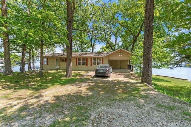ranch-style house with a water view, dirt driveway, a carport, a garage, and a front yard