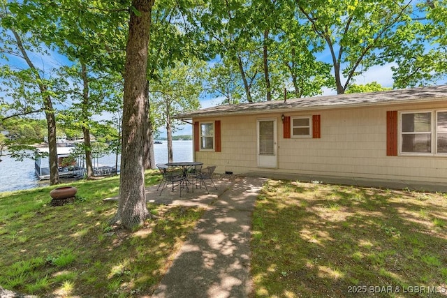 back of property with a water view, a lawn, roof with shingles, and a patio area