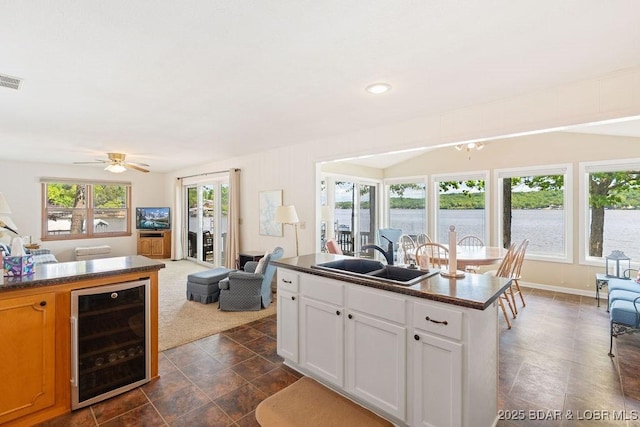 kitchen featuring wine cooler, open floor plan, a sink, dark countertops, and a ceiling fan