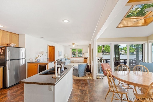 kitchen featuring freestanding refrigerator, beverage cooler, a ceiling fan, a sink, and dark countertops