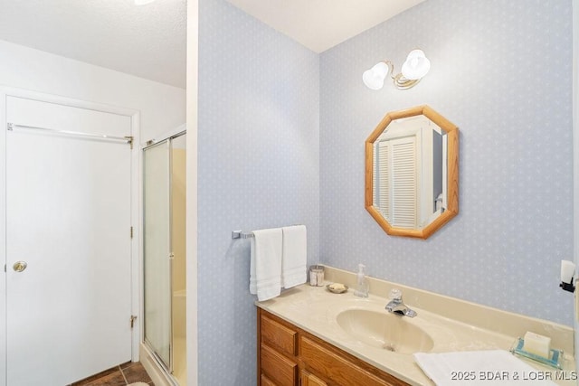 full bathroom with a stall shower, vanity, and wallpapered walls