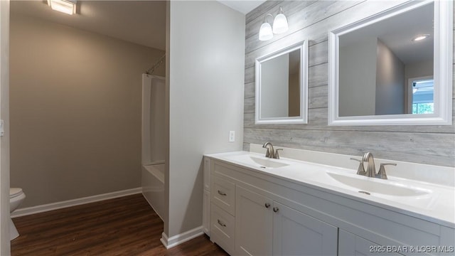 bathroom featuring toilet, wood finished floors, double vanity, baseboards, and shower / tub combo