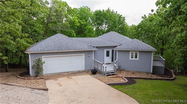 single story home featuring a shingled roof, a garage, driveway, and view of scattered trees