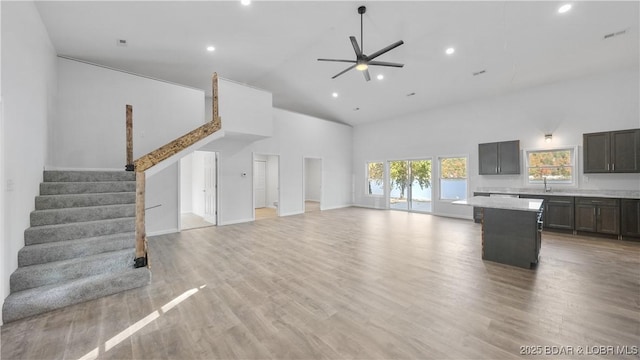 unfurnished living room with high vaulted ceiling, a sink, recessed lighting, a ceiling fan, and stairway