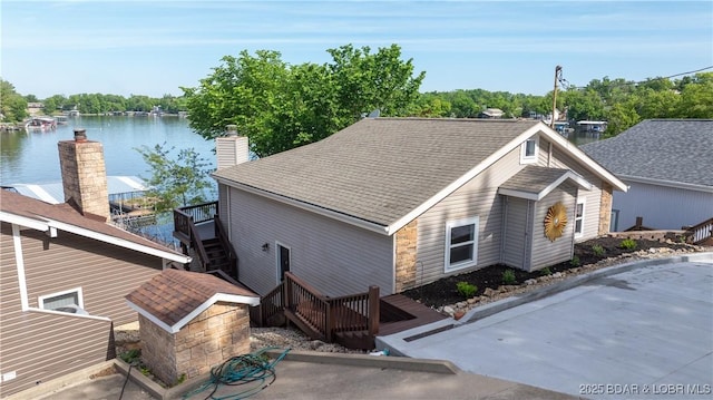 view of front of property with a shingled roof, stairs, a chimney, and a deck with water view