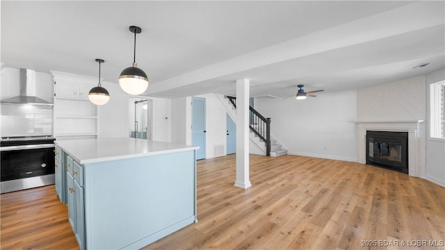 kitchen featuring wall chimney exhaust hood, oven, blue cabinets, light countertops, and a glass covered fireplace