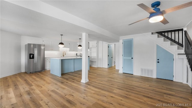unfurnished living room featuring light wood-style flooring, ceiling fan, stairs, baseboards, and a sink