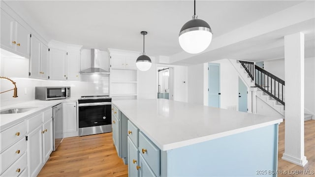 kitchen with wall chimney range hood, appliances with stainless steel finishes, a sink, and light wood-style floors
