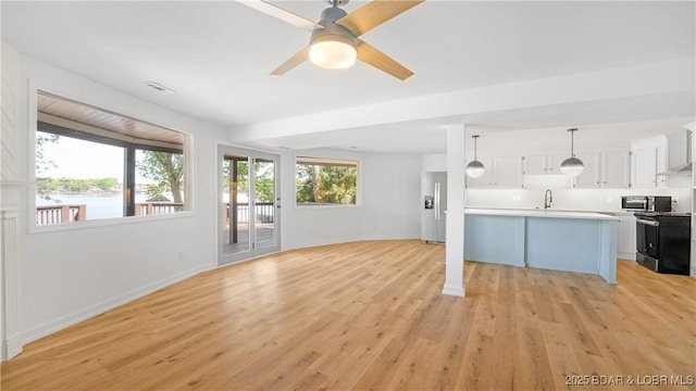unfurnished living room with baseboards, light wood-type flooring, ceiling fan, and a sink