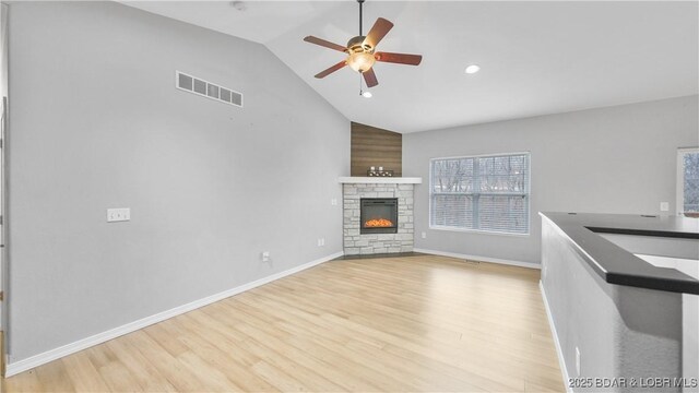unfurnished living room with ceiling fan, vaulted ceiling, light wood finished floors, a fireplace, and recessed lighting