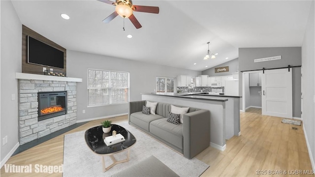 living area with a ceiling fan, lofted ceiling, a barn door, light wood finished floors, and baseboards