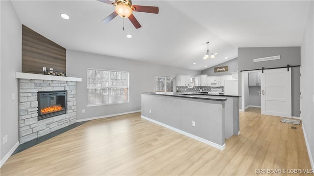 kitchen with a ceiling fan, a barn door, dark countertops, white cabinetry, and a fireplace