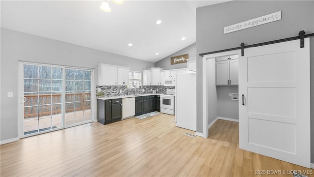 kitchen featuring white appliances, a barn door, white cabinets, light wood-style flooring, and decorative backsplash