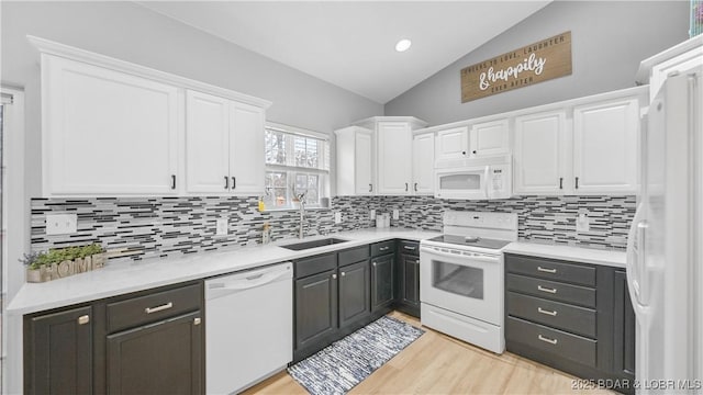 kitchen featuring white appliances, a sink, white cabinetry, lofted ceiling, and tasteful backsplash