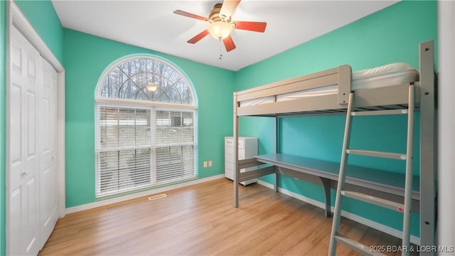 bedroom with baseboards, wood finished floors, a closet, and a ceiling fan