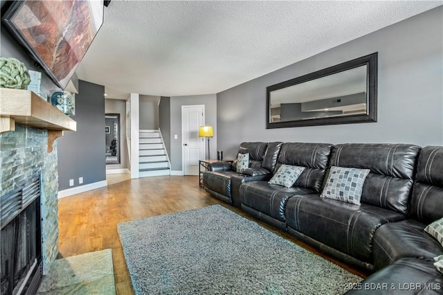 living room featuring a stone fireplace, wood finished floors, stairway, baseboards, and a textured ceiling