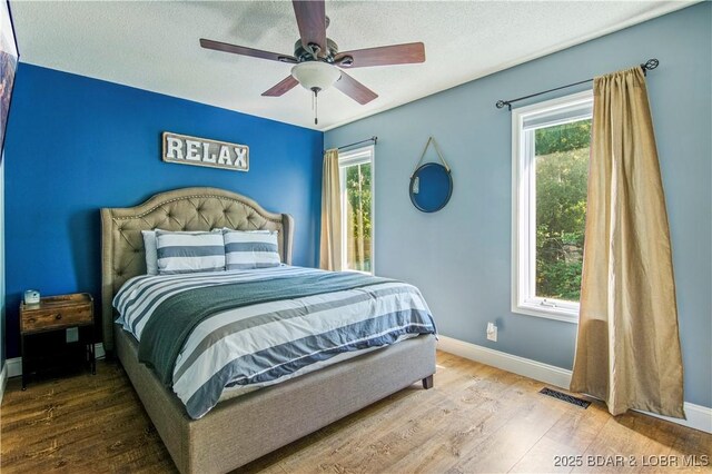 bedroom featuring multiple windows, wood finished floors, baseboards, a ceiling fan, and a textured ceiling