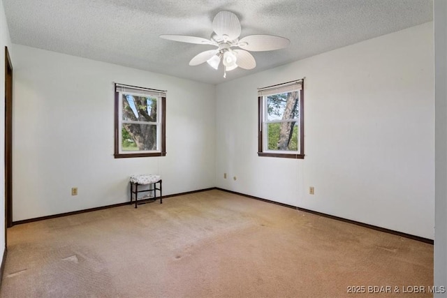 carpeted spare room featuring a textured ceiling, a ceiling fan, and baseboards