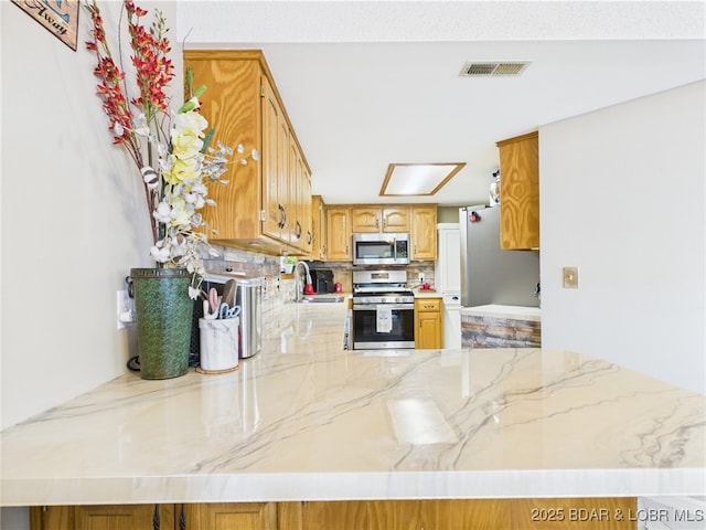 kitchen with appliances with stainless steel finishes, a sink, a peninsula, light stone countertops, and decorative backsplash
