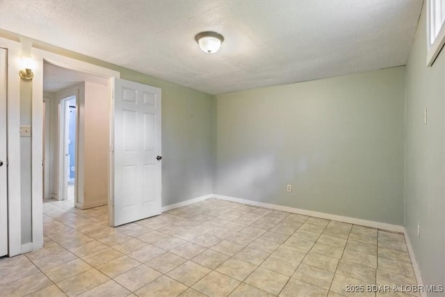 unfurnished room with light tile patterned floors, baseboards, and a textured ceiling