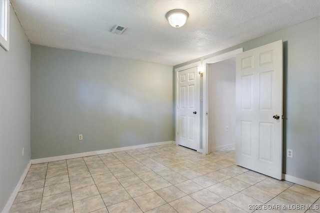 empty room featuring a textured ceiling, light tile patterned floors, and baseboards