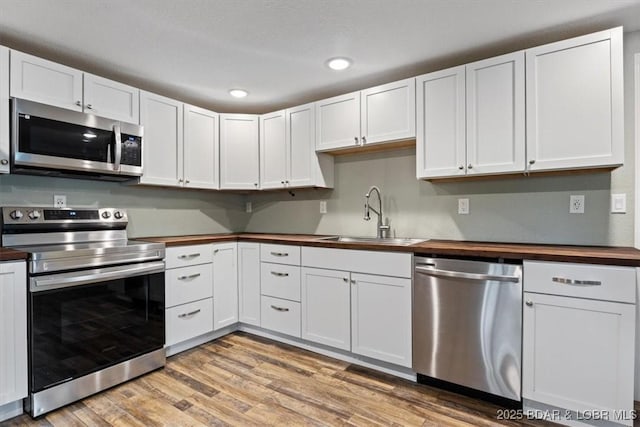 kitchen featuring stainless steel appliances, butcher block counters, a sink, light wood-style floors, and white cabinetry