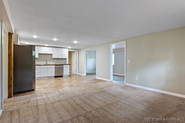 unfurnished living room with recessed lighting, baseboards, light carpet, a sink, and light wood-type flooring