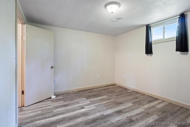 empty room featuring wood finished floors, a textured ceiling, and baseboards