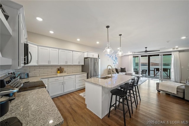 kitchen with appliances with stainless steel finishes, open floor plan, a sink, tasteful backsplash, and dark wood-style flooring