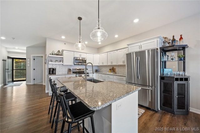 kitchen with appliances with stainless steel finishes, a sink, open shelves, white cabinets, and baseboards