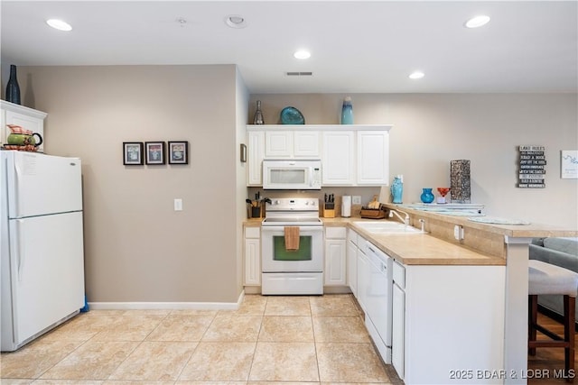 kitchen with white appliances, a peninsula, a sink, a breakfast bar area, and white cabinets