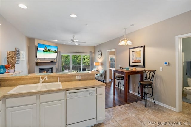 kitchen with white dishwasher, a sink, open floor plan, a glass covered fireplace, and white cabinetry