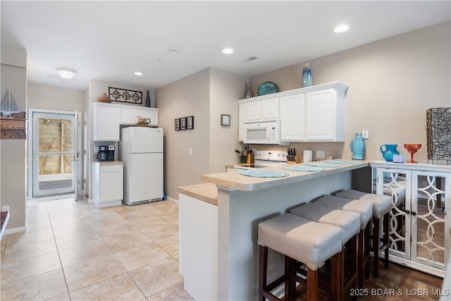 kitchen with white appliances, light countertops, a peninsula, white cabinets, and a breakfast bar area