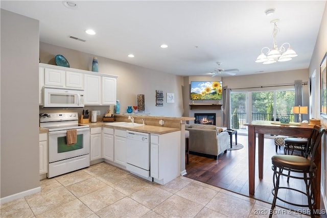 kitchen with white appliances, a peninsula, a glass covered fireplace, open floor plan, and recessed lighting