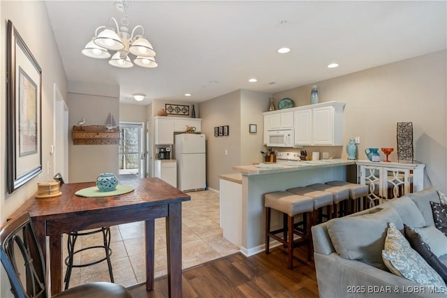 kitchen with white appliances, a peninsula, white cabinets, a chandelier, and recessed lighting