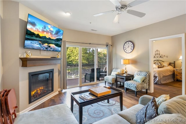 living room with wood finished floors, a glass covered fireplace, and ceiling fan
